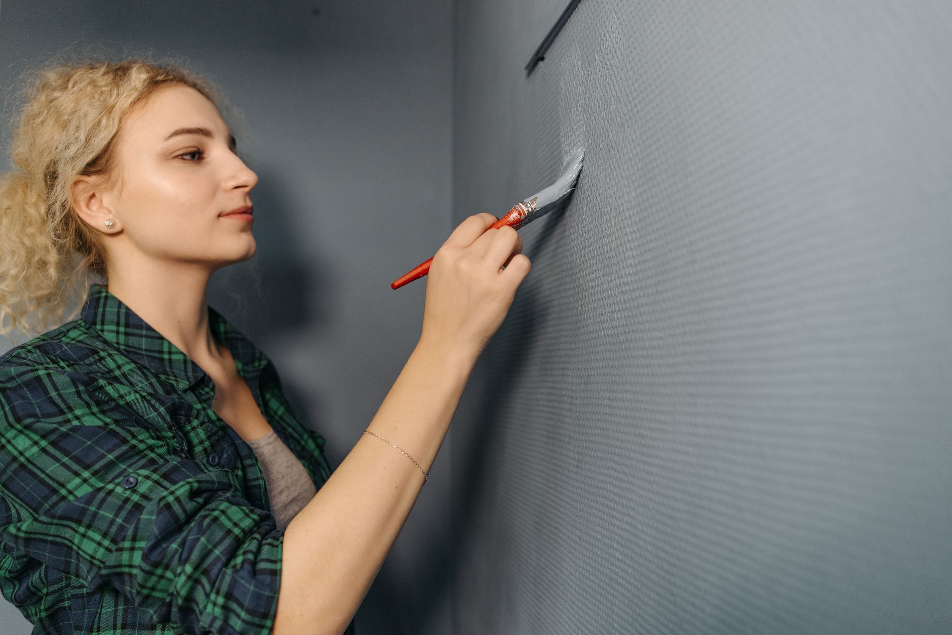 A woman in a plaid shirt painting a gray wall indoors, focusing on home improvement in Torrance, CA